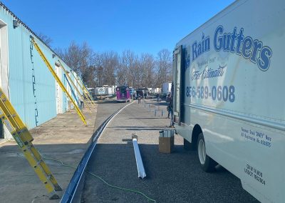 The Van's Rain Gutters truck parked by a building. There are several yellow ladders leading against the building